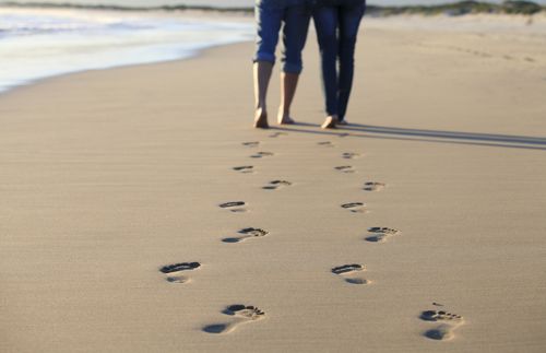 couple walking on beach, leaving footprints in the sand