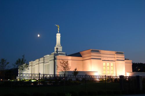 The entire Spokane Washington Temple lit up at night, with a view of the moon in the background.