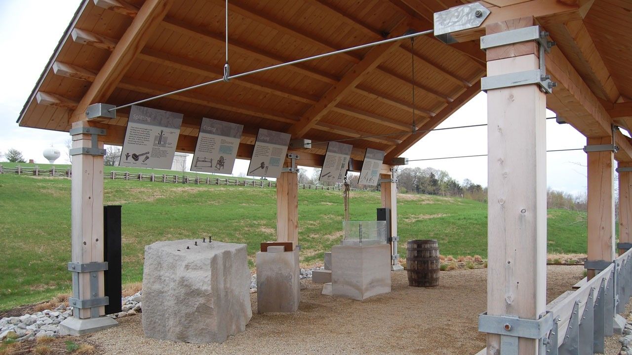 Five instructional panels, large stone blocks, and a barrel located underneath a wood pavilion. 