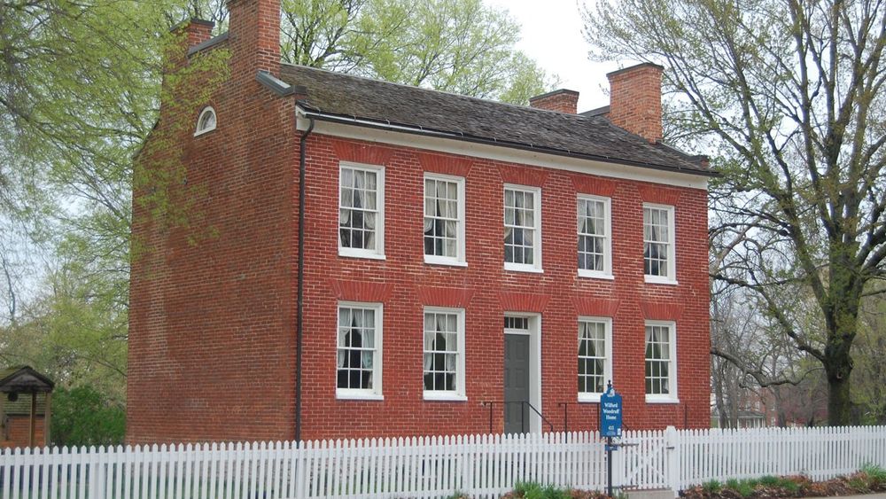 A two-and-a-half-story brick home with a white picket fence.