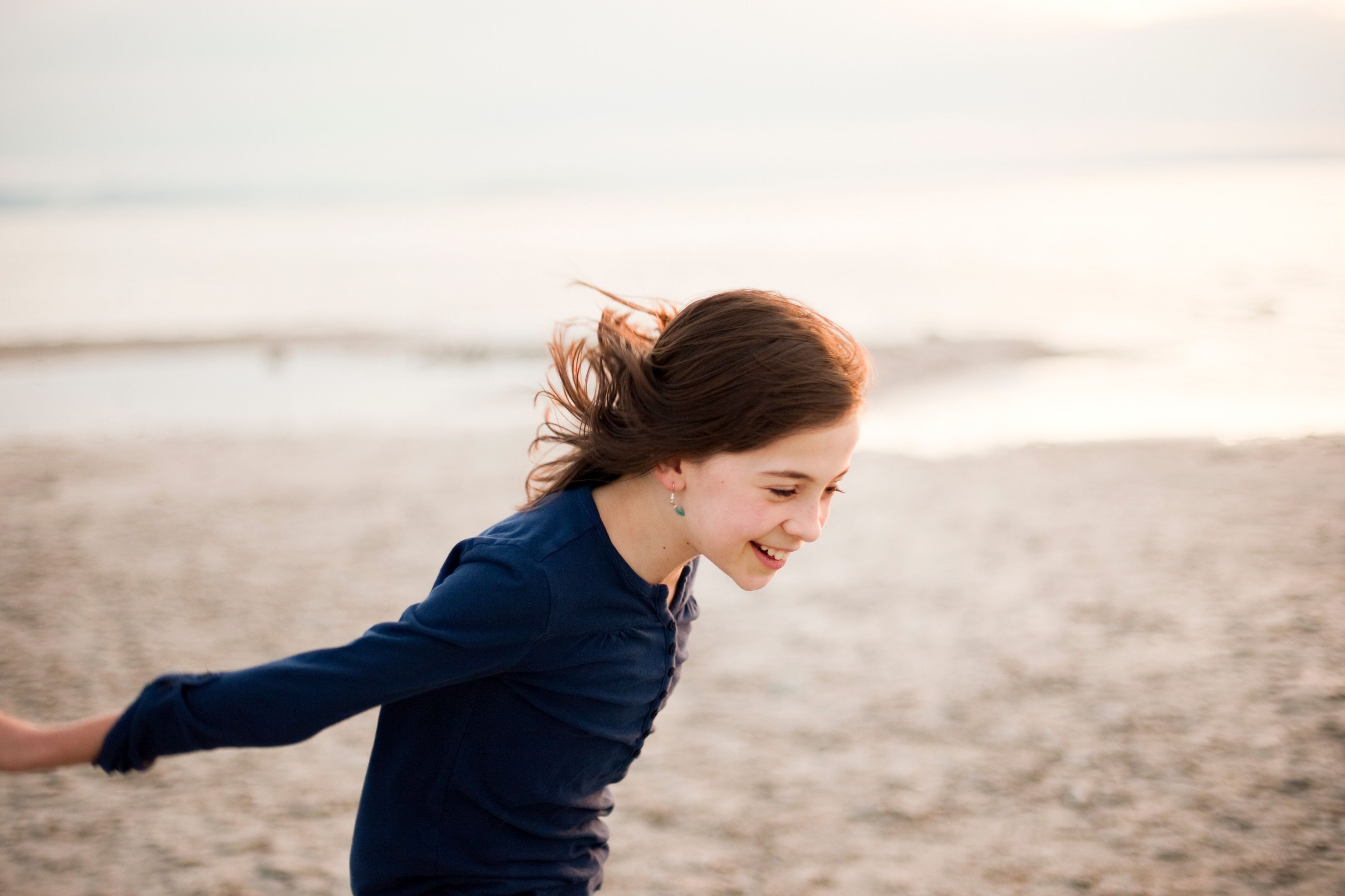 A young girl runs on the beach, with sand and water in the background.