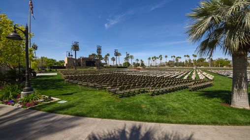 Chairs on a grass lawn in front of an outdoor stage. 