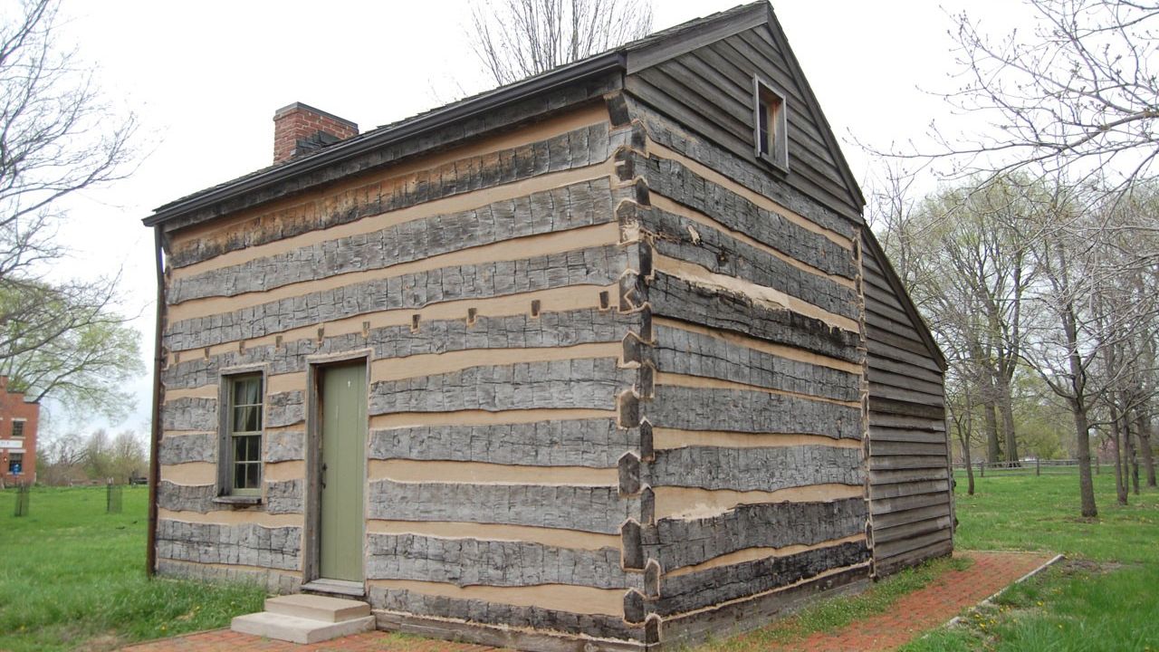 Small replica log cabin and a lean-to addition on the back and a brick path leading to the door.