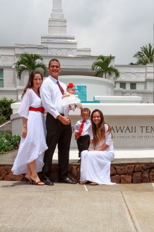 A mother and two daughters in white dresses with a father and son in white shirts and red ties standing outside the Kona Hawaii Temple after being sealed.