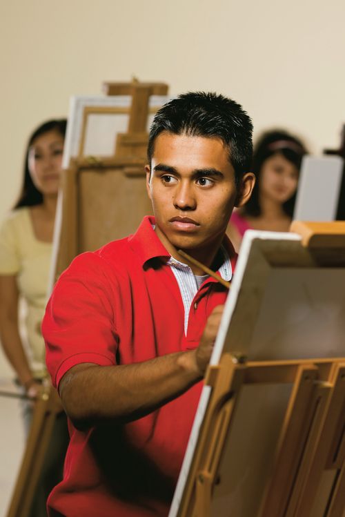 A male art student painting as he looks away at a model or object that he is painting.