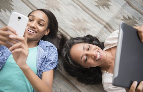 mother and daughter lying on carpet using cell phone and digital tablet