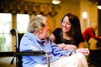 A young woman visting with an elderly woman in a wheelchair.