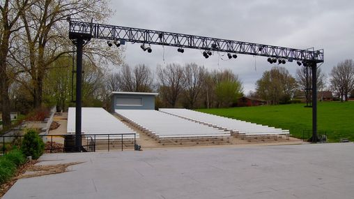 View from a stage looking out at rows of bleachers. Theater lighting is at the front of the stage.