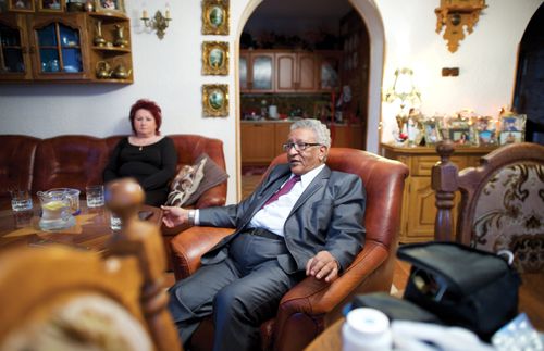 Michael sitting in a chair and his wife, Renata, sitting on a couch in a living room.