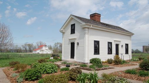 One-and-a-half-story, central chimney, white clapboard home with a well-landscaped surroundings.