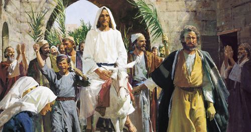 Jesus Christ in white robes riding on a white donkey. He is passing through a brick arch into Jerusalem. Numerous people are following Him. Some of which are waving palm leaves and laying cloth on the ground in front of Him.