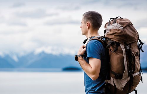 A young adult man wearing a backpack looking out over a lake