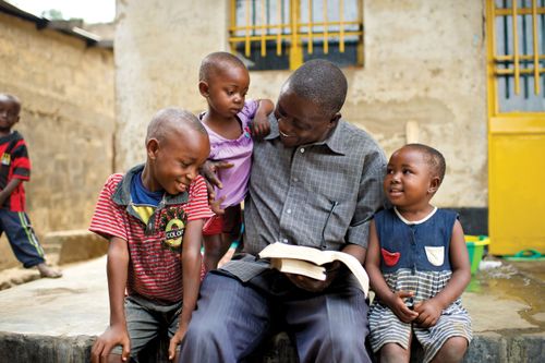 A father and his three young children in the Congo sit outside and open a set of scriptures together to read.