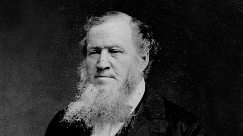 Head and shoulders portrait of Brigham Young in his seventies. He is depicted with a long beard and wearing a dark suit.
