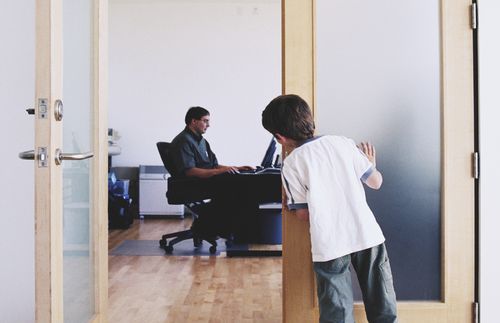 boy watching father from doorway of office