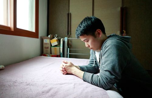 young man kneels by his bedside