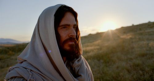Actor portraying Jesus Christ is standing on a hillside as the sun rises over the horizon.