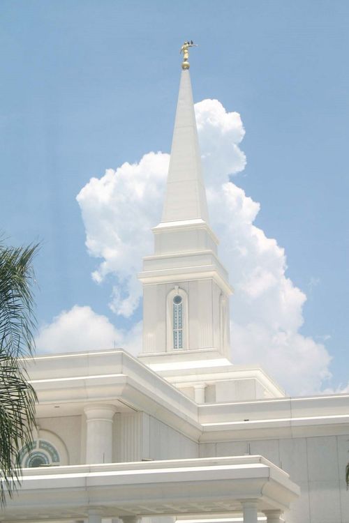 The spire of the Orlando Florida Temple and the angel Moroni statue set against a blue sky with fluffy white clouds.