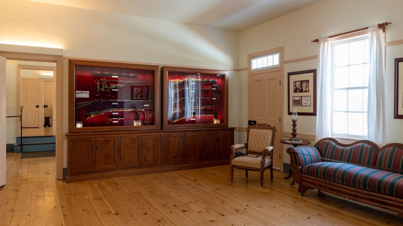 Interior view of several gun cabinets mounted to a wall. Inside are historic rifles and pistols and a cavalry saber.