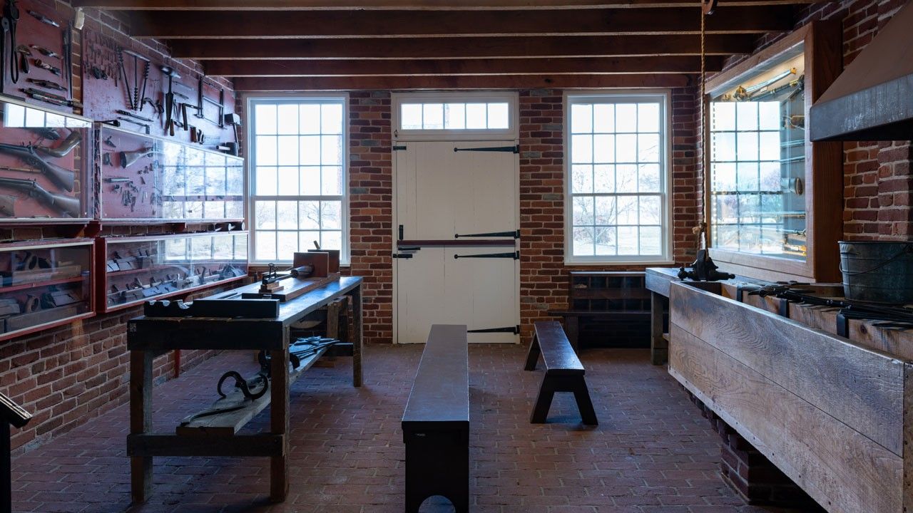 View of an unlit brick forge with several iron tools lined up in a row.