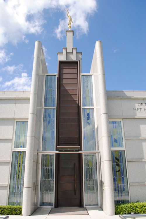 The front entrance of The Hague Netherlands Temple, with a view of windows, doors, and the angel Moroni on the spire.