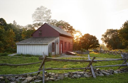 Photograph of a red clapboard house with a rail fence in the foreground and sunset in the background.