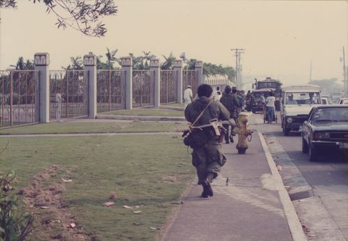 Soldiers with guns walking away from the camera alongside the temple’s fence.