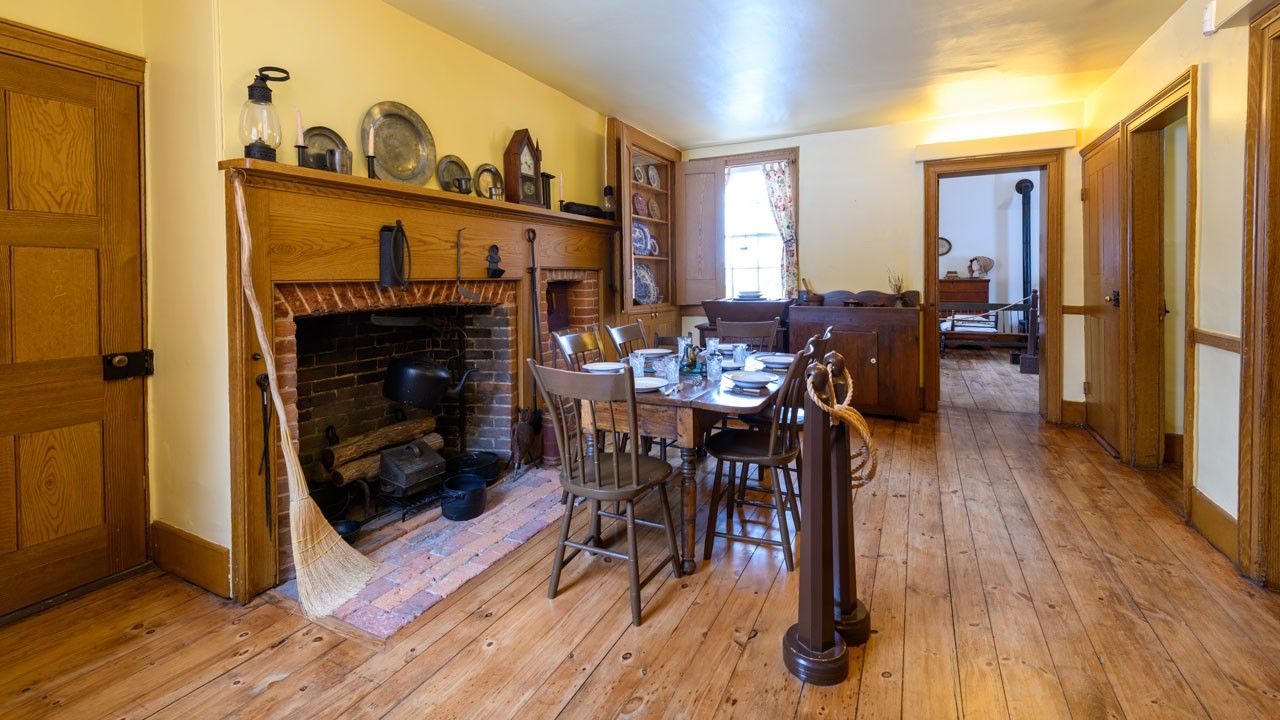 A dining room interior with wood floor and chairs surrounding a table and a large fireplace. 