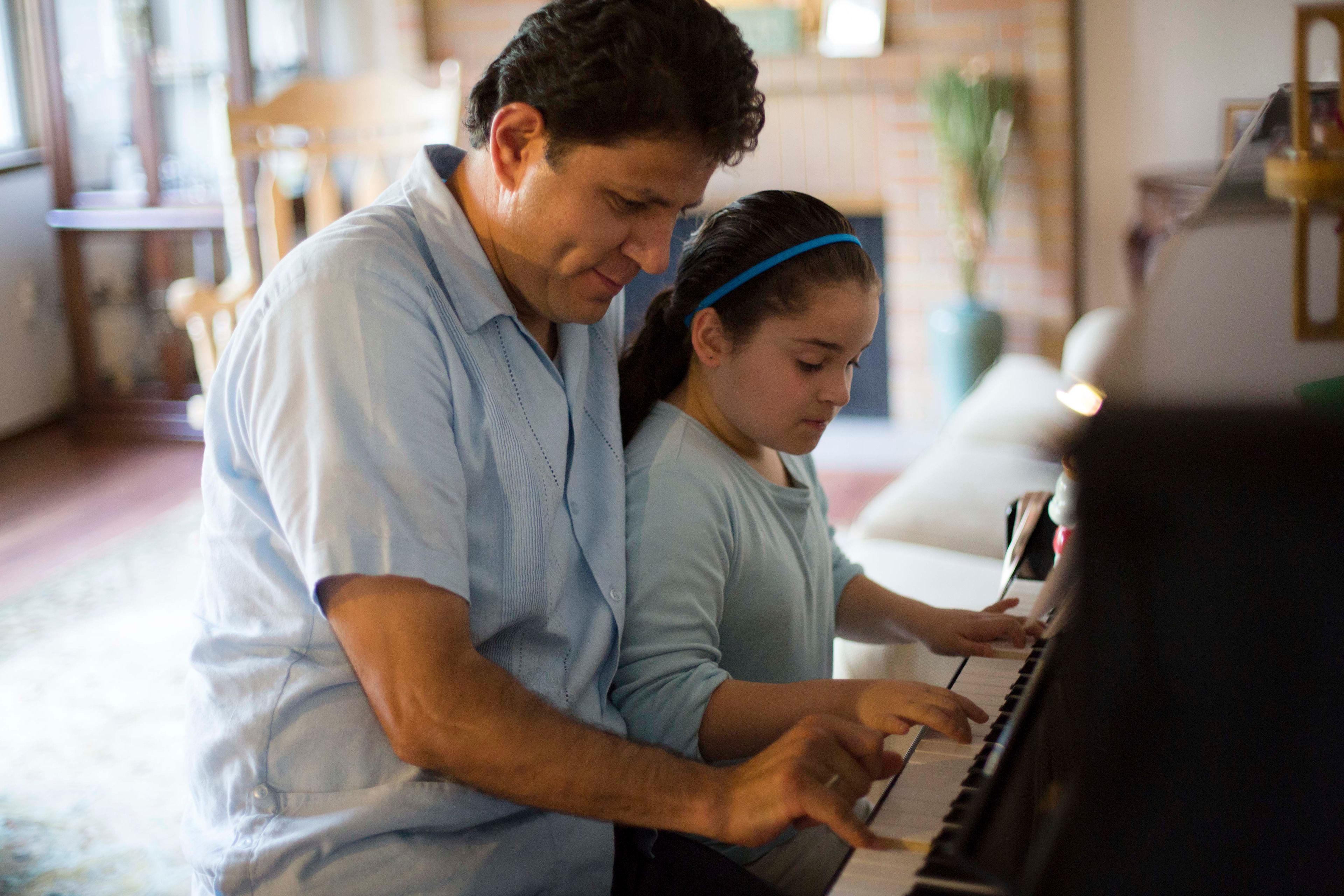 A father plays the piano with his daughter.