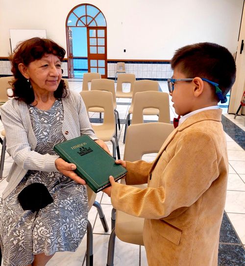 Rafael passing out a hymnbook to a woman at church.