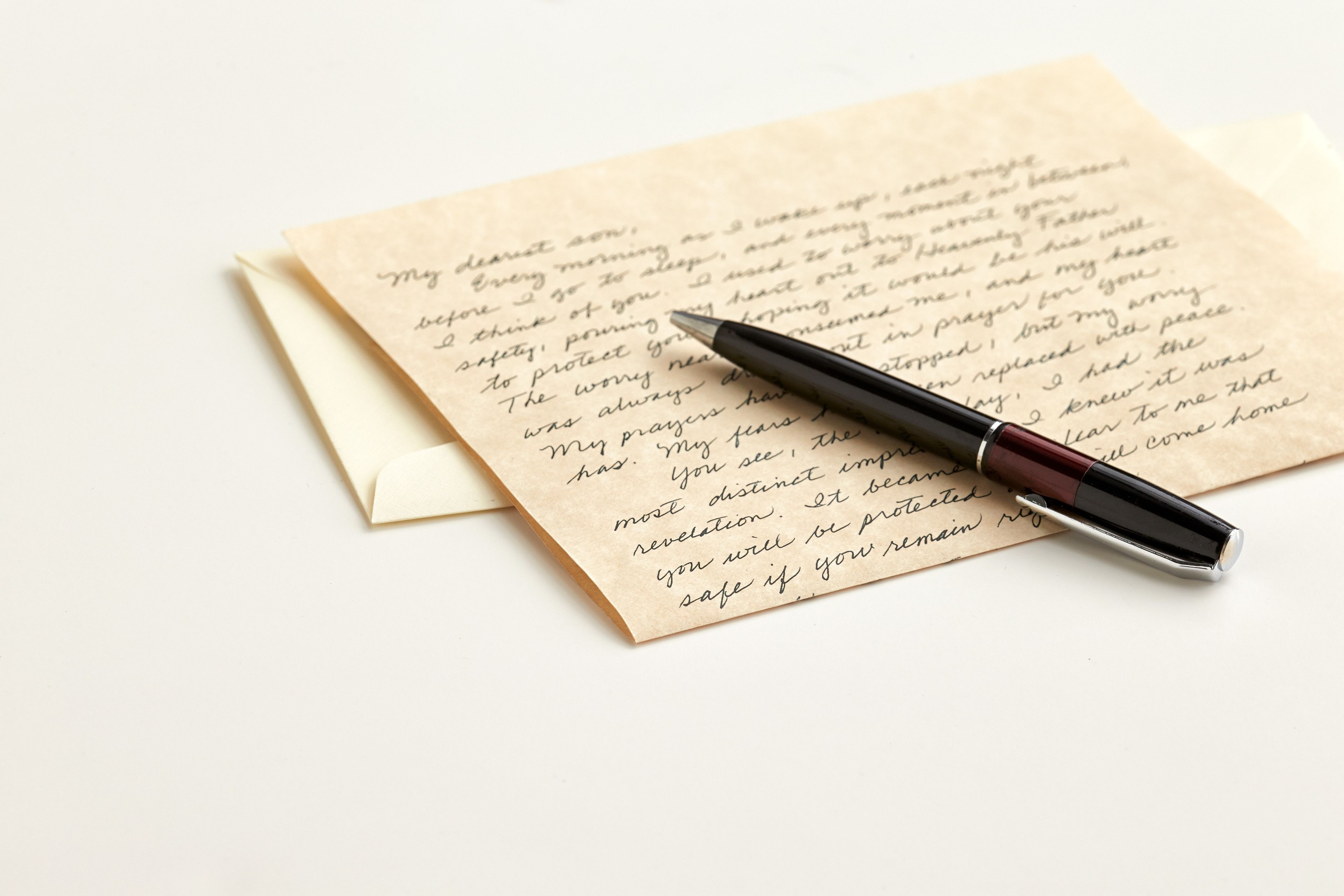 A handwritten letter lying on a white surface with an envelope and a pen.