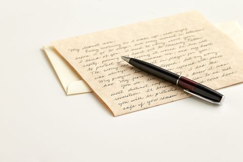 A brown pen lying on top of a handwritten letter and an envelope.