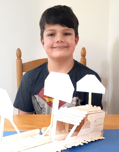 Boy holding boat made out of craft sticks