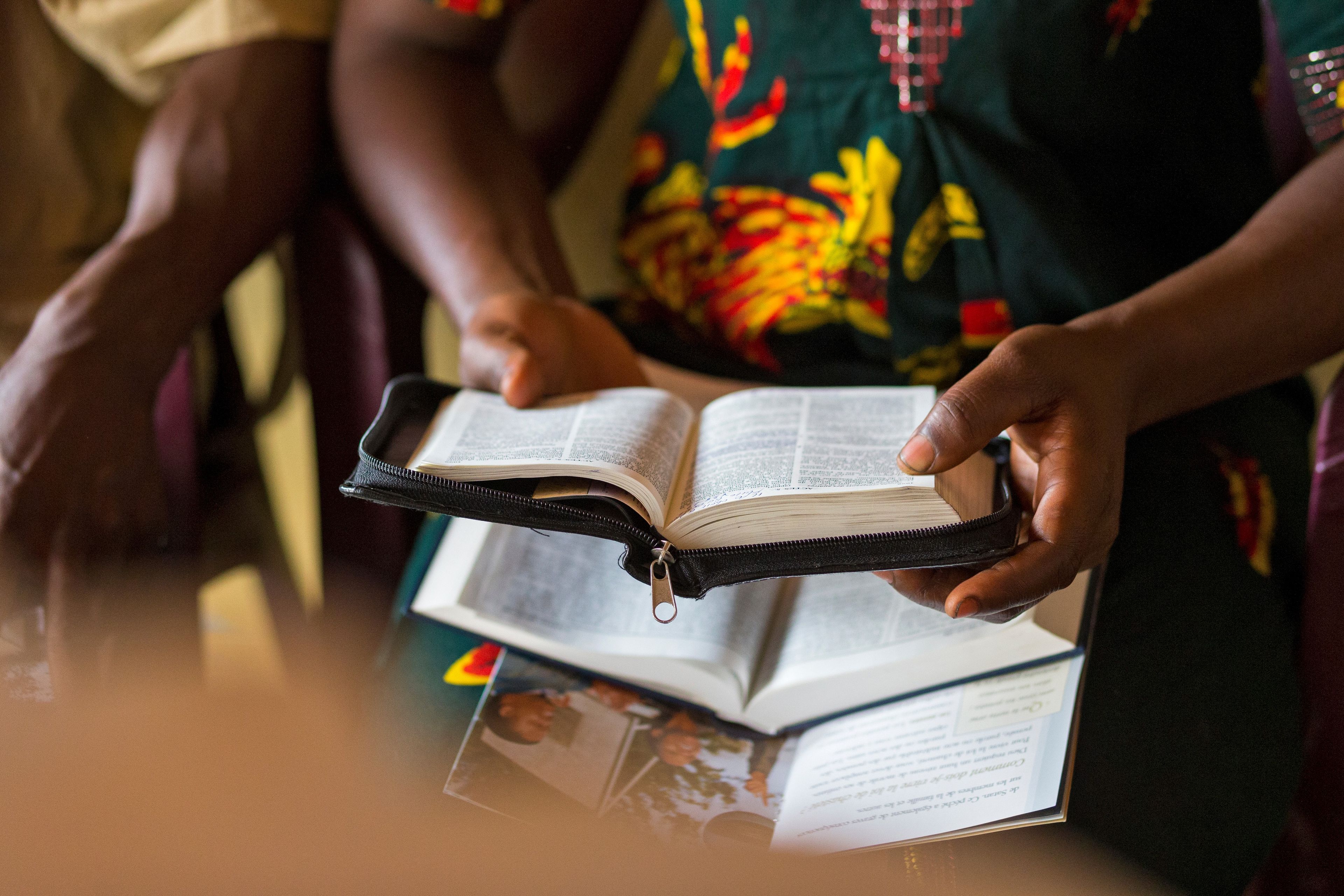 A woman holds open a set of scriptures in her hands. Another set is on her lap.