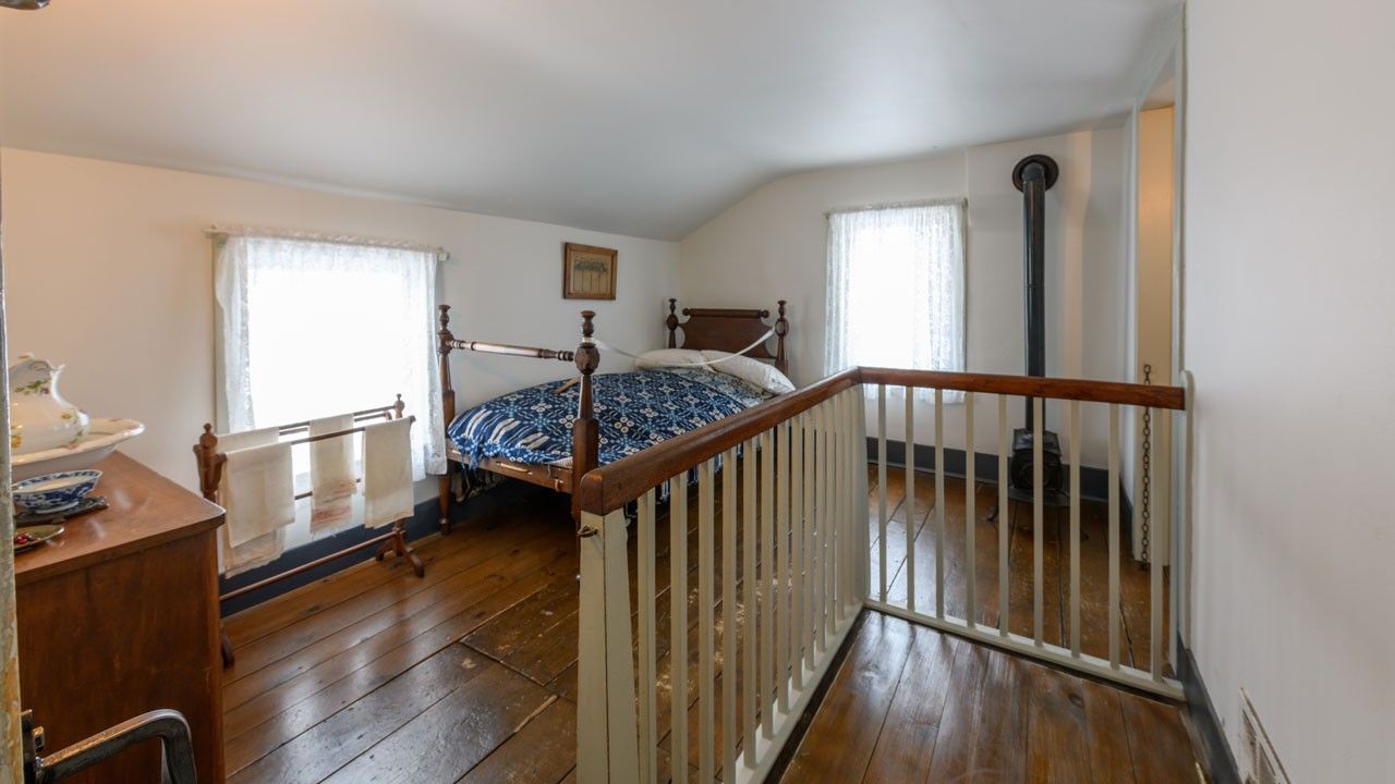 Interior room with a small bed in the corner. There are white wood railings in the foreground.