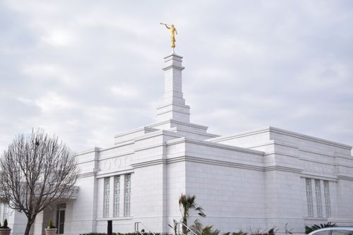 An exterior side view of the Ciudad Juárez Mexico Temple, including the angel Moroni, against a cloudy sky.