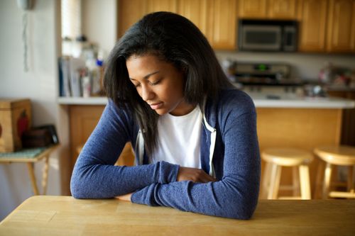 A young woman folds her arms and rests them on a table while she prays.