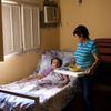 woman with food tray standing next to a woman lying in bed