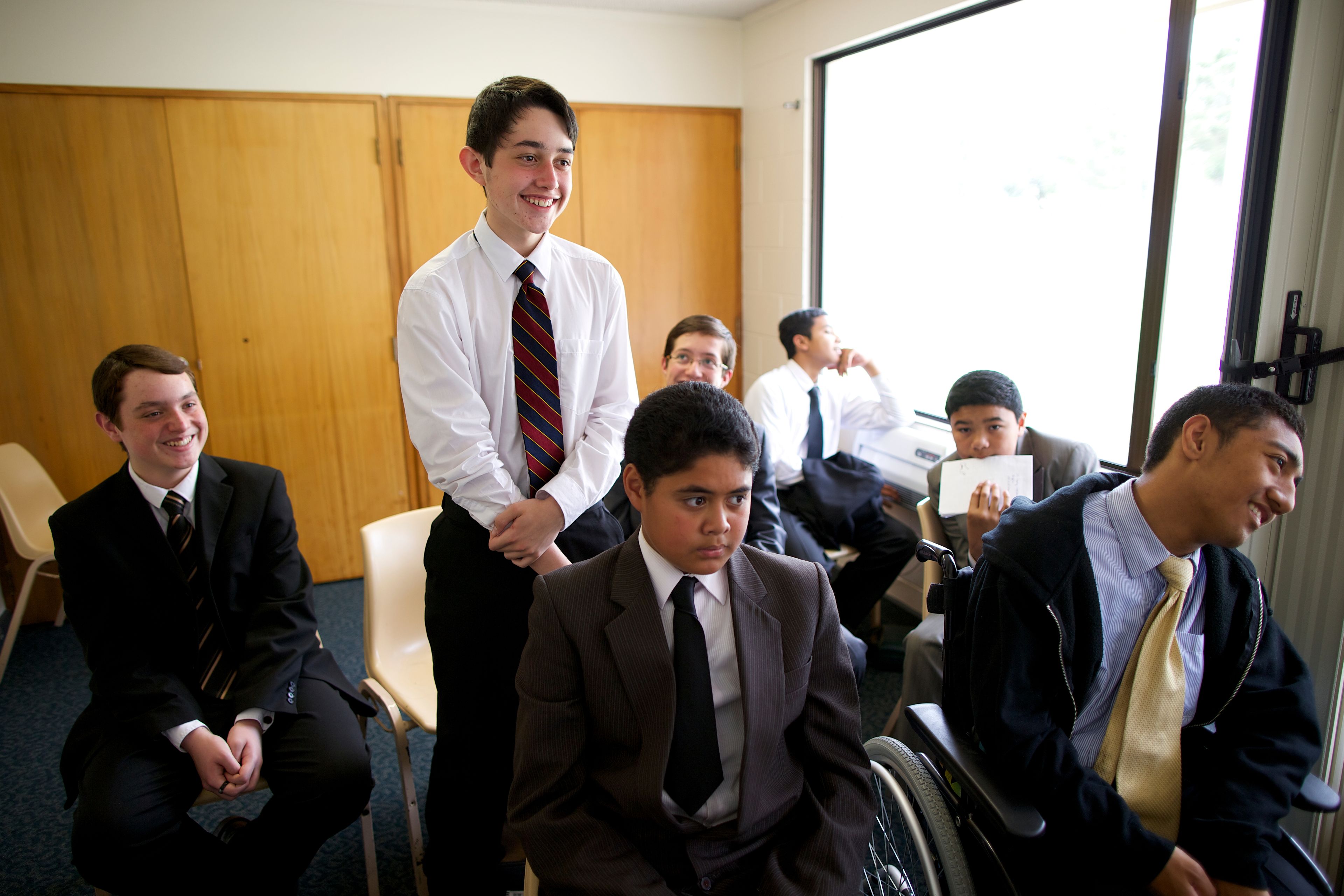 A young man stands up during priesthood meeting, surrounded by his classmates.  