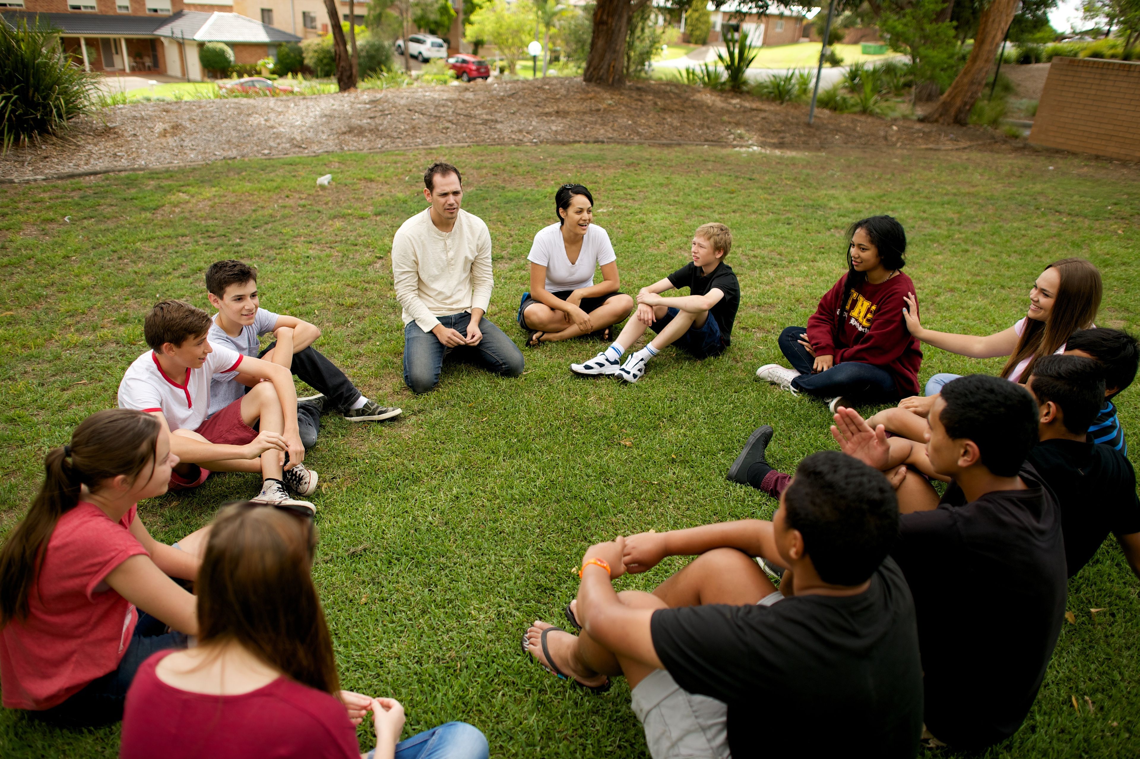 A group of youth sitting in a circle in a yard and playing games together.