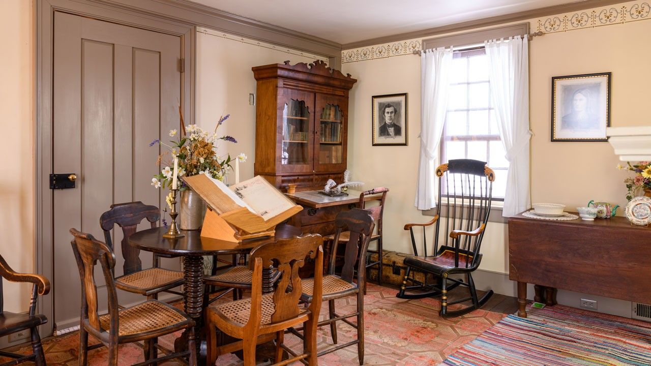 An interior with a large open book on a table surrounded by chairs and a large gray door.