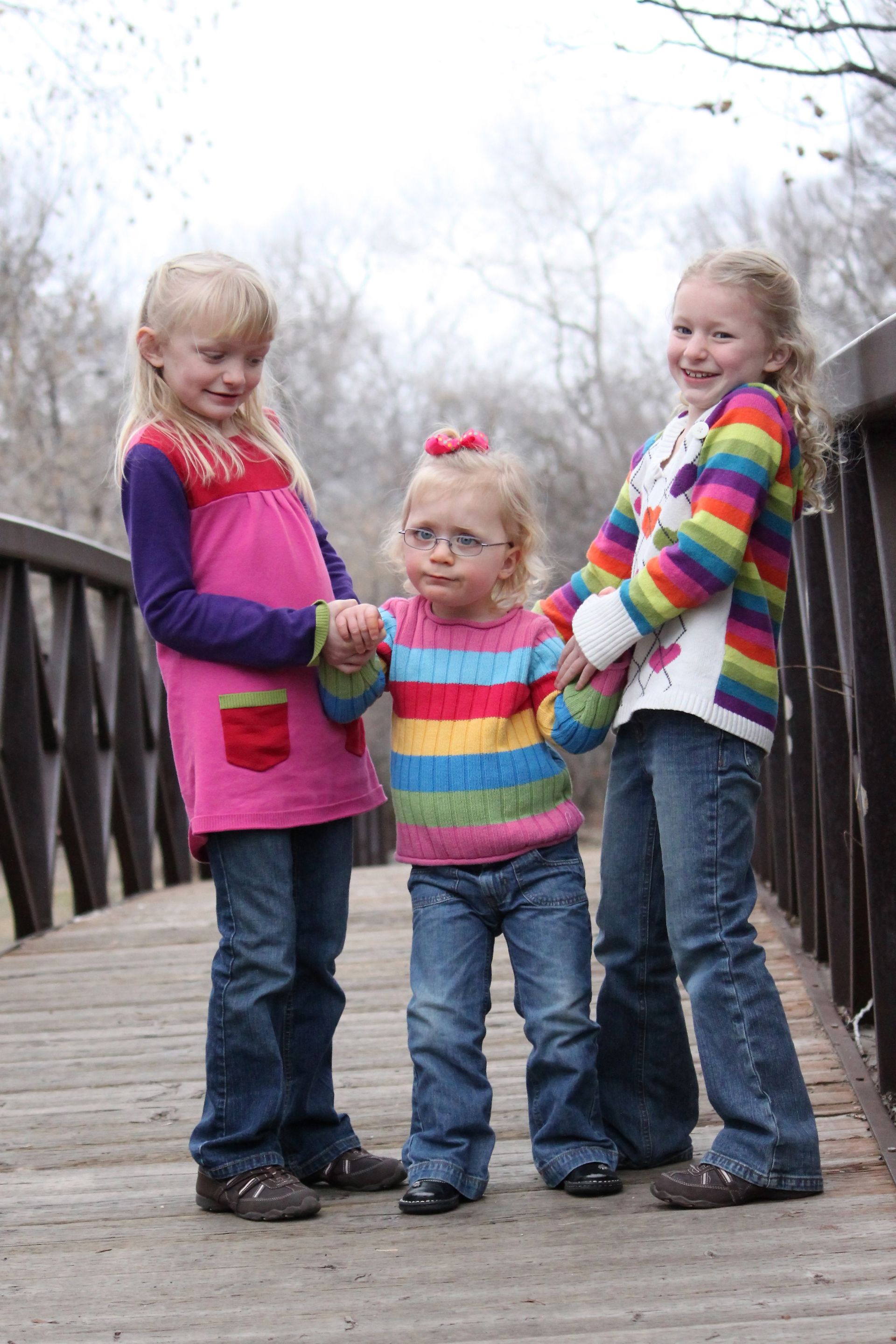 Three young sisters standing on a bridge together.