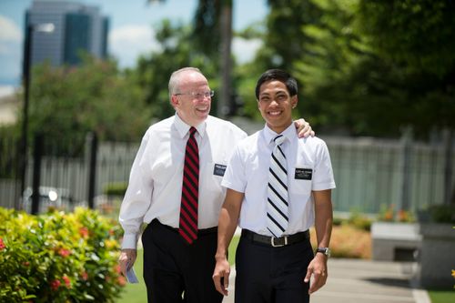 A senior elder missionary rests his hand on the shoulder of an elder missionary as they smile and walk together in the Philippines.