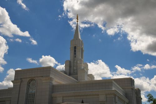 The spire on the Bountiful Utah Temple during the daytime, with a blue sky and white clouds in the background.