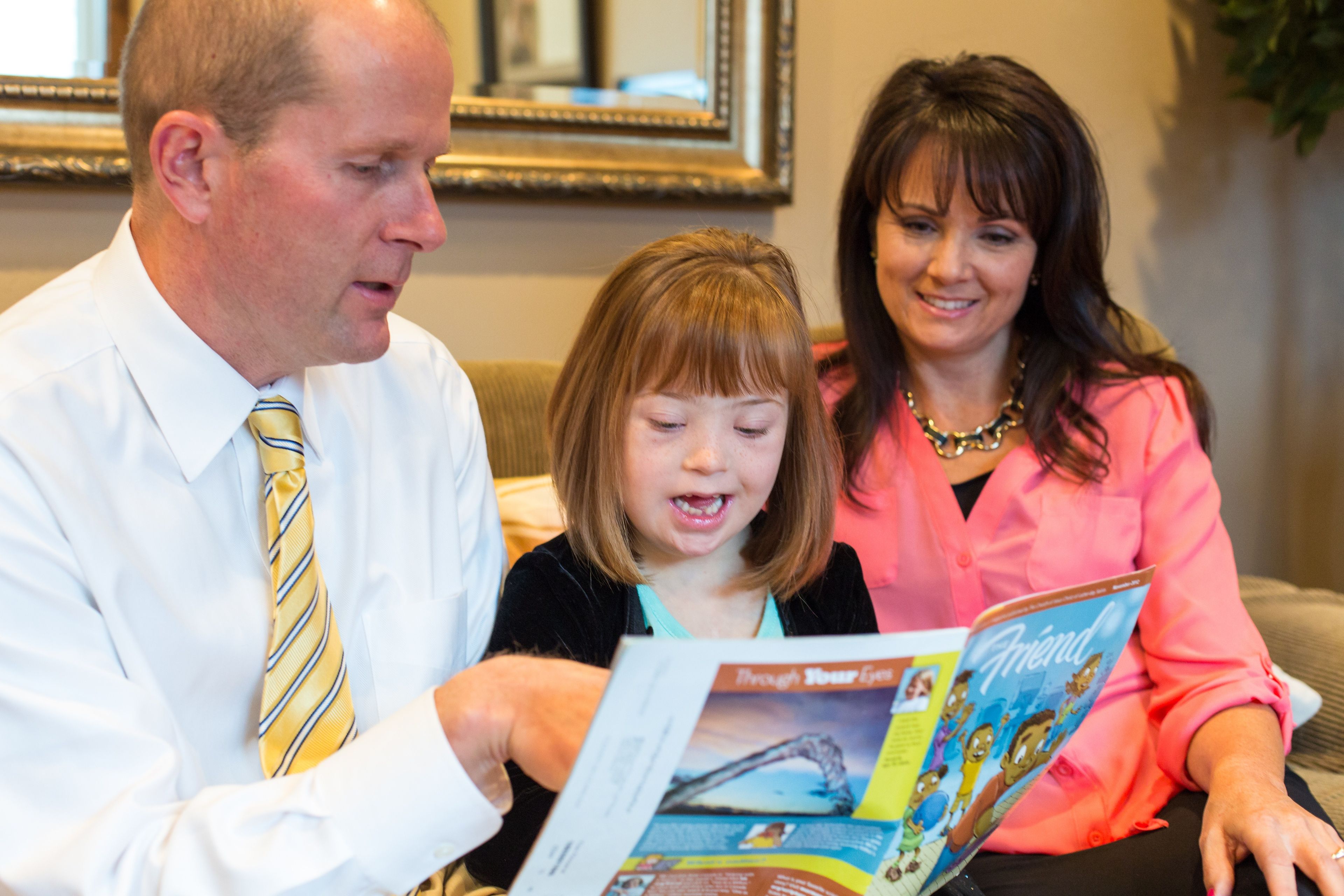 A mother and father read the Friend magazine with their young daughter.