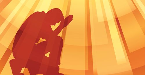 Silhouette of a man kneeling in prayer.  Rays of light are around him.