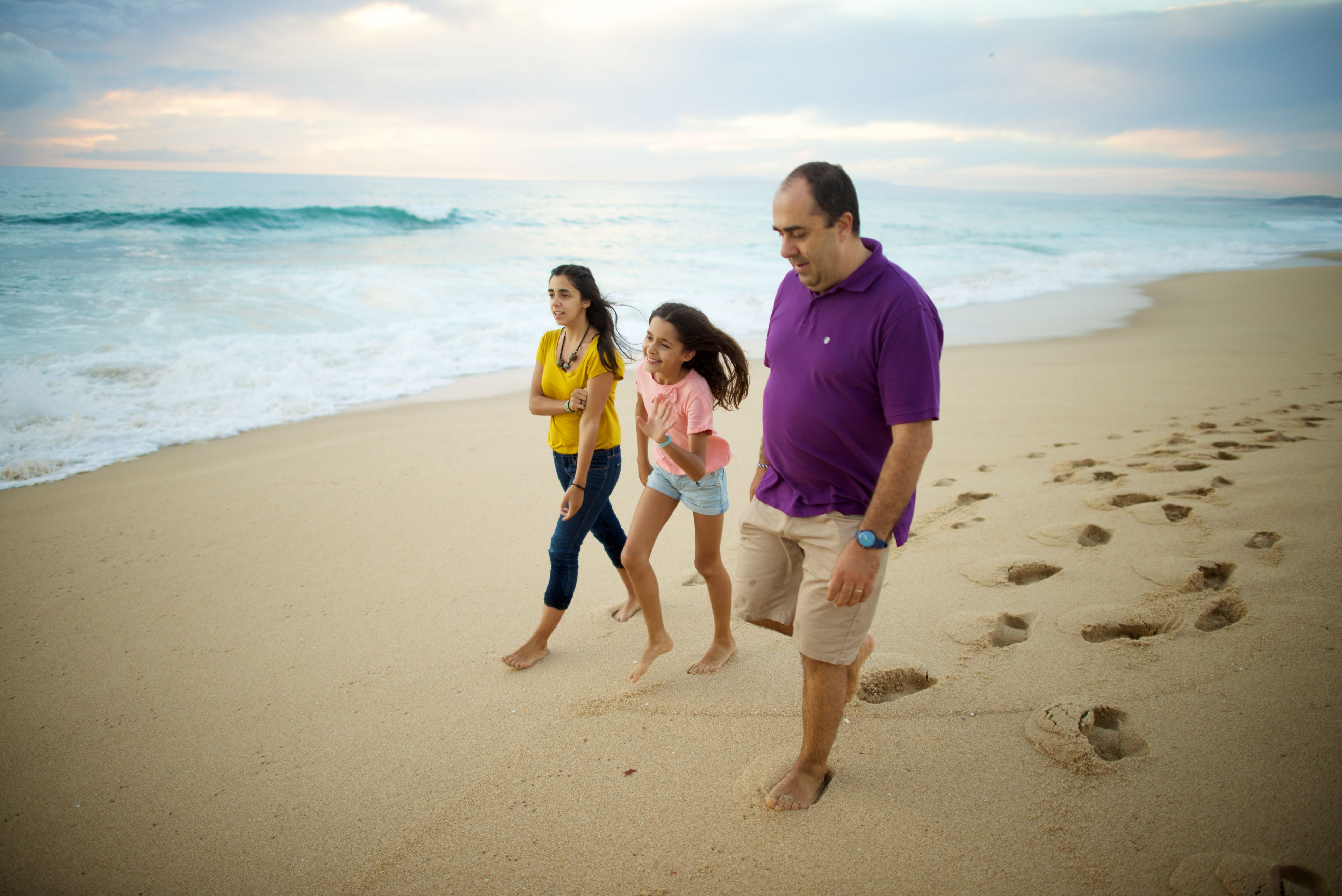 A father and two daughters walk together along the beach.