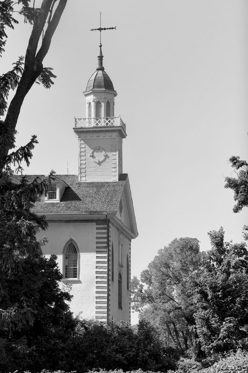 A black and white side view of the front half of the Kirtland Temple, with the branches of a tree on the left-hand side.