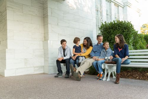 A father, mother, two sons, and two daughters talking and sitting on white benches outside the Raleigh North Carolina Temple.