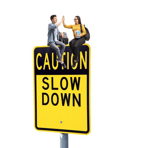 boy and girl atop a large “Slow Down” sign